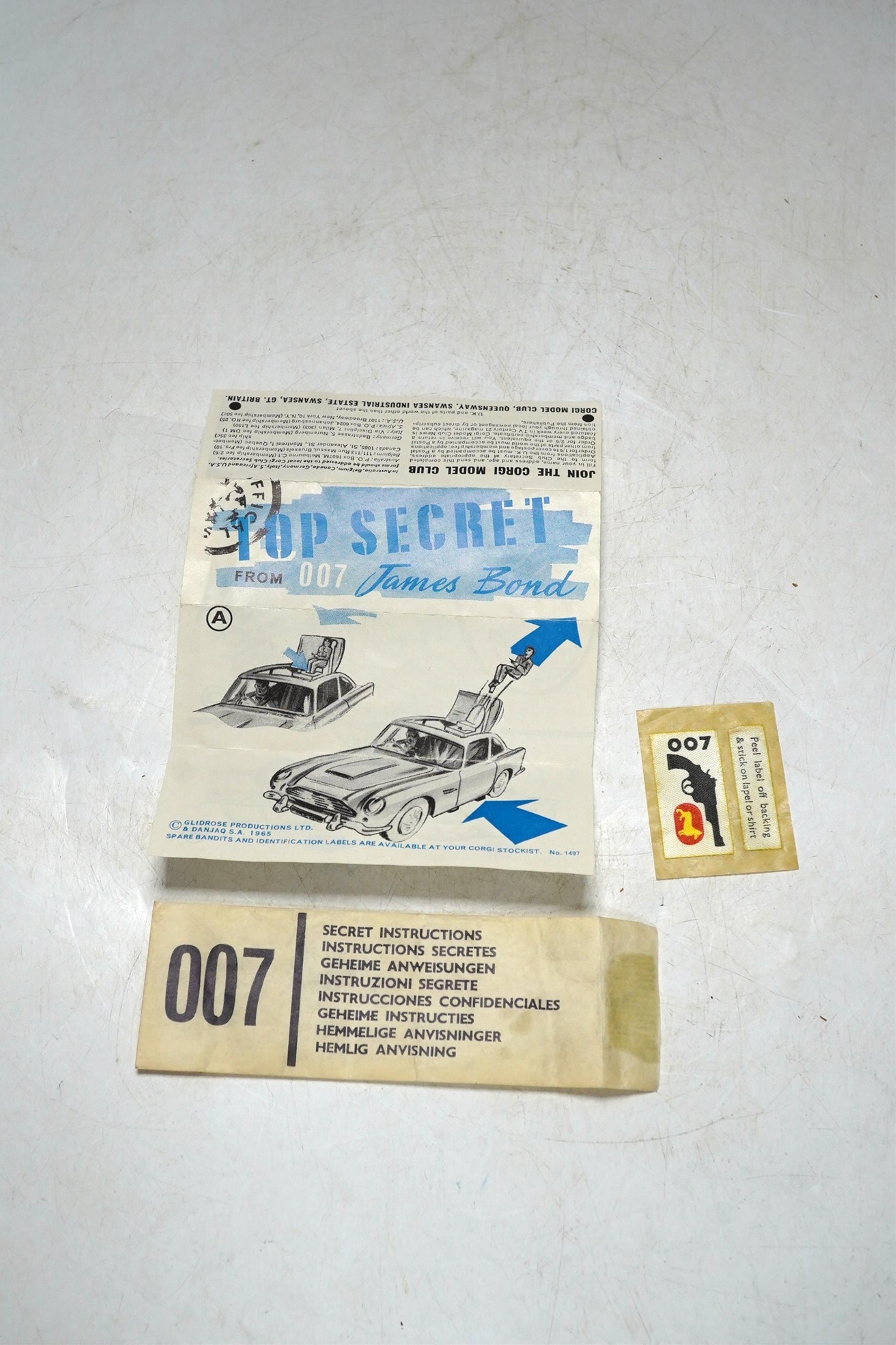 A boxed Corgi Toys James Bond 007 Aston Martin (261), a first issue example in gold finish, boxed with inner display stand, envelope for secret instructions, top-secret leaflet, sheet of two unused lapel stickers, and th